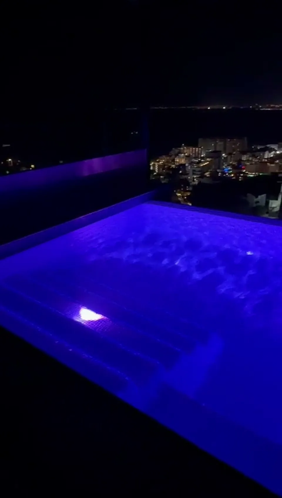 Alberca con iluminación LED de noche y la ciudad encendida al fondo