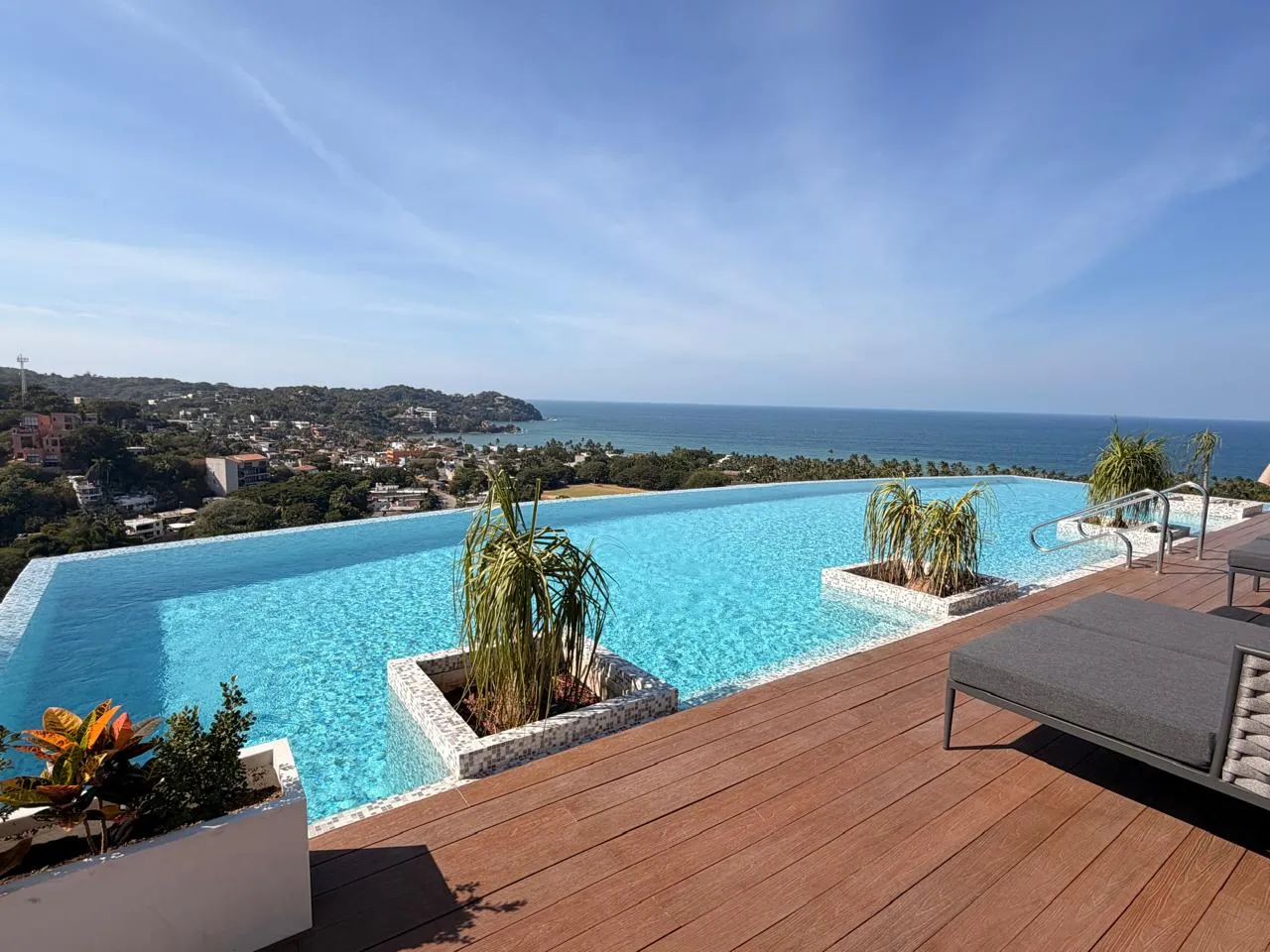 Alberca turquesa con jardineras y deck de madera frente al mar