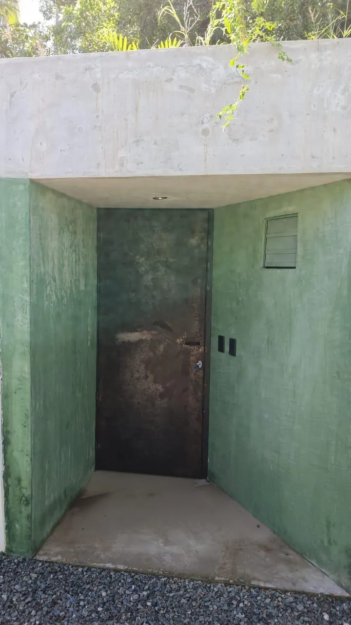 Acceso con muros de concreto verde y puerta de acero