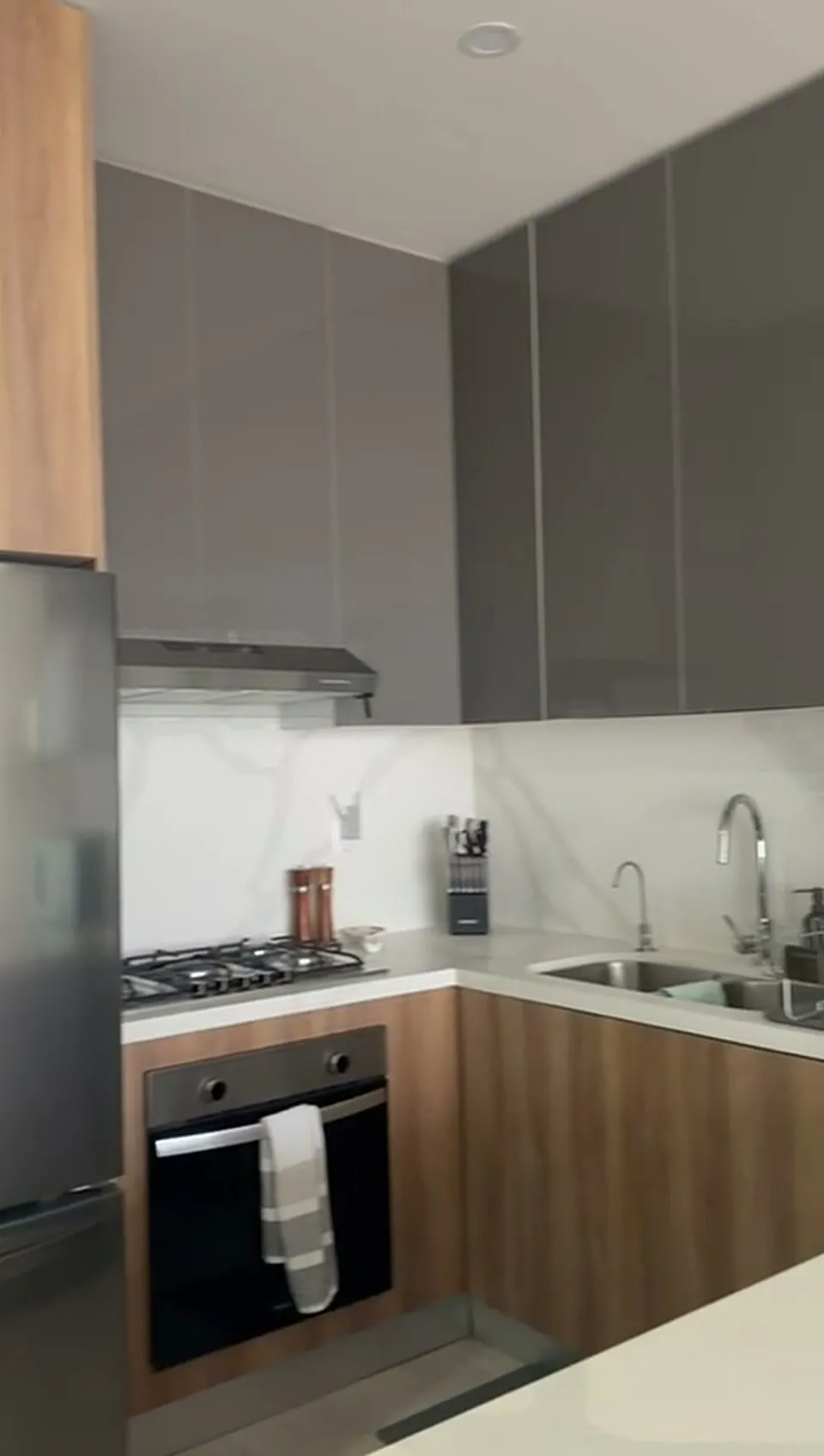Cocina con gabinetes en gris y nogal, horno y parrilla empotrados